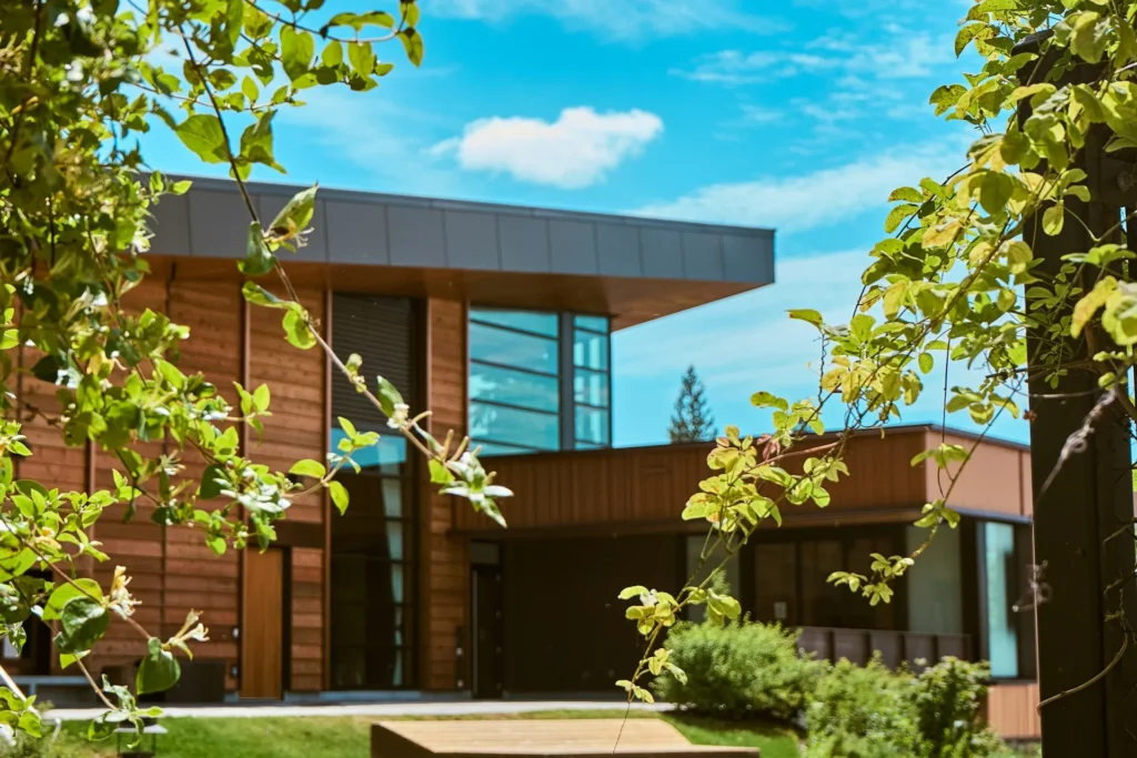 Modern flat-roofed home exterior surrounded by trees under blue sky.